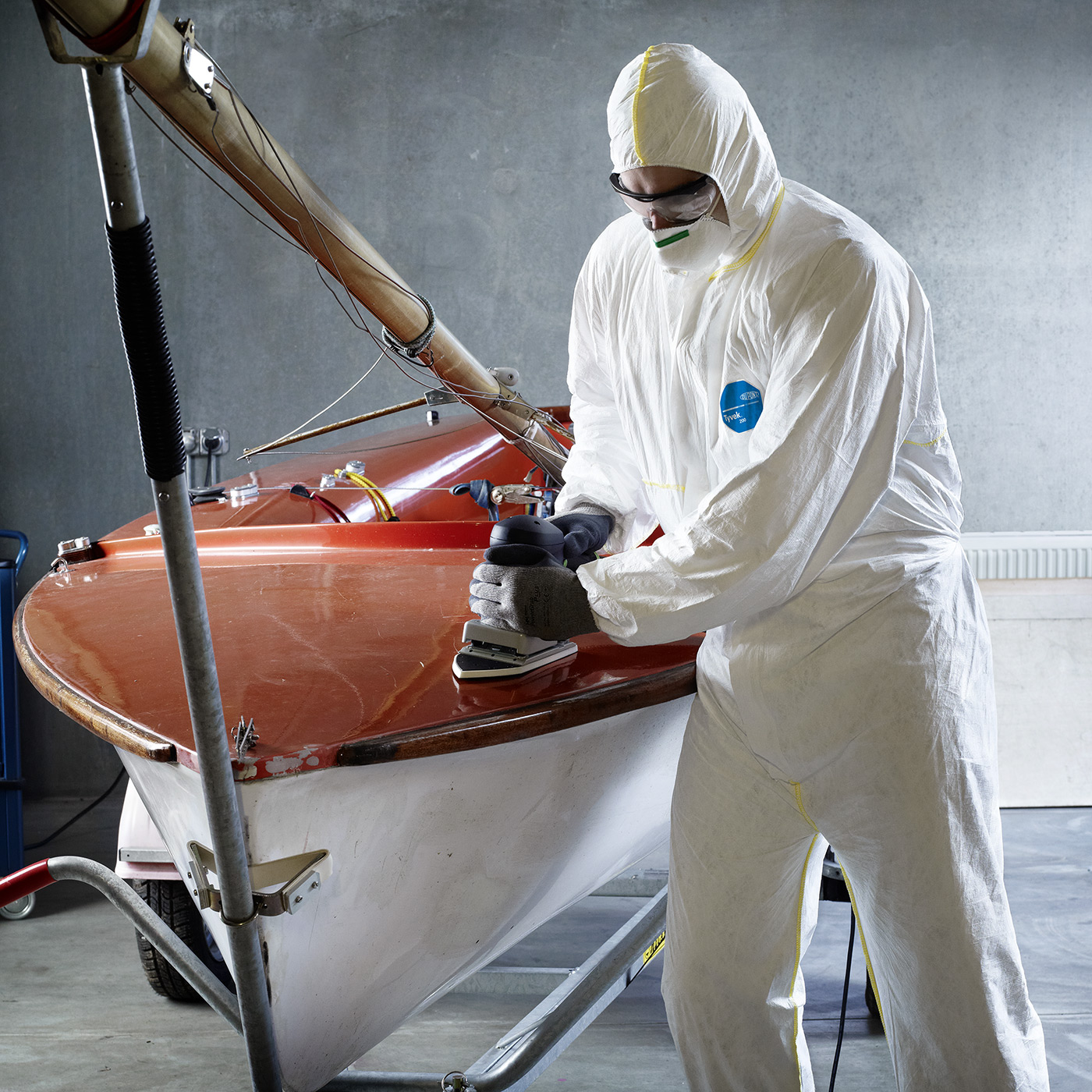 Person im DuPont Tyvek 200 Easysafe Overall mit Atemschutzmaske schleift einen Bootsrumpf